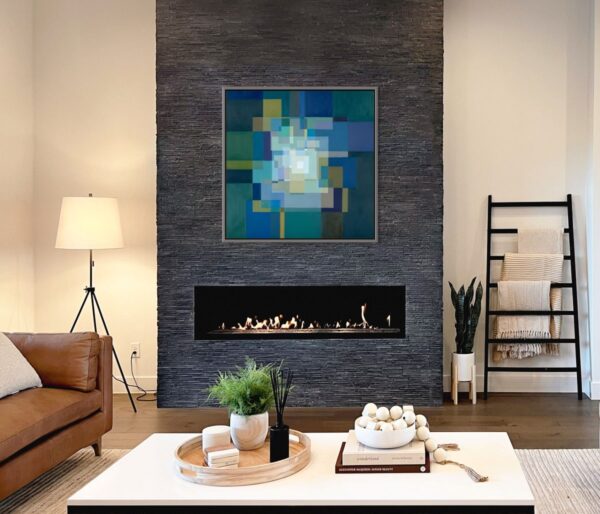Framed abstract painting of a menorah in soft blue shades with a glowing center, symbolizing light, faith, and renewal, displayed in a modern interior