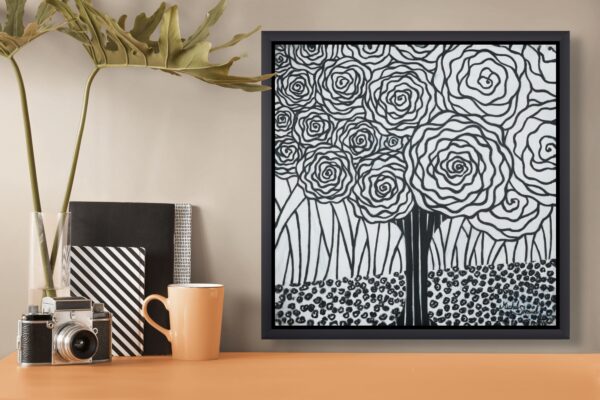 Framed black and white abstract tree artwork with spiral flowers, displayed on desk with vintage camera, notebooks, and orange mug